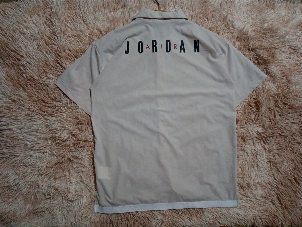 Jordan Short Sleeve Button-Up Shirt (Category: Tshirts & Polo Shirts ) located in Boston. Submitted by johnpaulvi30029 (Listing ID 1465692760, Image 2). Description: - Authentic Jordan short sleeve button-up shirt in beige - Features snap front closure and classic collar - Red Jumpman logo on left chest with large black and red Jordan lettering on the back - Stylish white striped trim along the bottom hem - DM for measurements or more details, tr