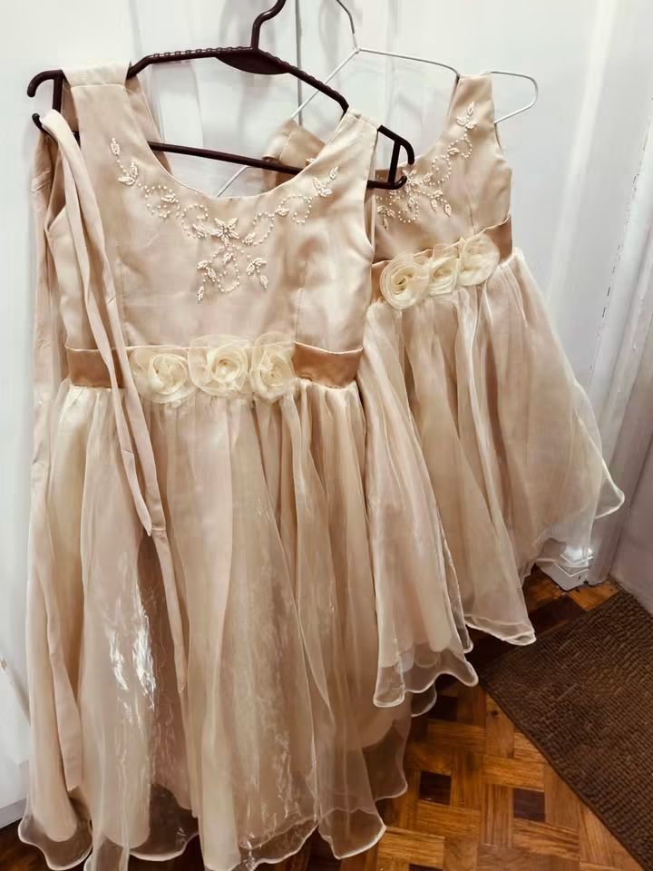 Kids gown (Category: Babies & Kids Fashion) located in Manila. Submitted by iccythng0216 (Listing ID 1465601263, Image 1). Description: - Matching champagne gold dresses for siblings (worn once sa wedding) - Sizes: Two different sizes included in the set - Details: Beaded necklines and flower appliques at the waist - Design: Tulle skirts over white lining with back zipper and tie sashes - Ideal for: Weddings, pageants, and special occasions - Con