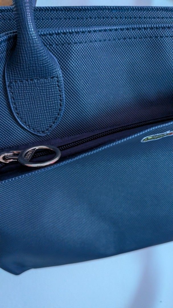Lacoste Navy Blue Hand and Shoulder Bag (Category: Tote Bags) located in Quezon City. Submitted by maff_mallow (Listing ID 1465599605, Image 3). Description: - Color: Dark Blue - Material: Textured Saffiano-style exterior - Straps: Double top handles and a detachable shoulder strap - Branding: Signature embroidered crocodile logo on the front pocket - Interior: Cream-colored fabric with repeating Lacoste text and crocodile graphics - Compartments