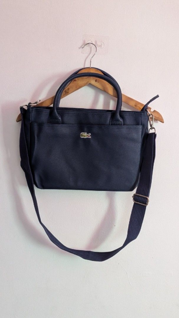 Lacoste Navy Blue Hand and Shoulder Bag (Category: Tote Bags) located in Quezon City. Submitted by maff_mallow (Listing ID 1465599605, Image 1). Description: - Color: Dark Blue - Material: Textured Saffiano-style exterior - Straps: Double top handles and a detachable shoulder strap - Branding: Signature embroidered crocodile logo on the front pocket - Interior: Cream-colored fabric with repeating Lacoste text and crocodile graphics - Compartments