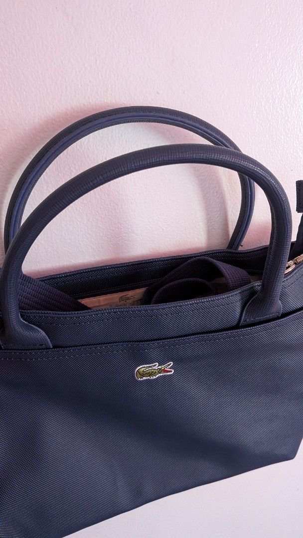 Lacoste Navy Blue Hand and Shoulder Bag (Category: Tote Bags) located in Quezon City. Submitted by maff_mallow (Listing ID 1465599605, Image 2). Description: - Color: Dark Blue - Material: Textured Saffiano-style exterior - Straps: Double top handles and a detachable shoulder strap - Branding: Signature embroidered crocodile logo on the front pocket - Interior: Cream-colored fabric with repeating Lacoste text and crocodile graphics - Compartments