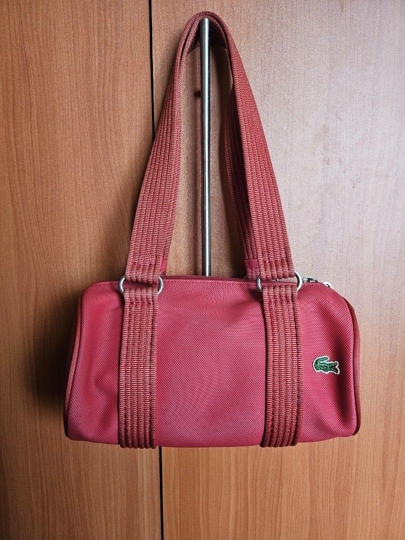 Lacoste Red Shoulder Barrel Bag (Category: Shoulder Bags) located in Mandaluyong City. Submitted by ohwmaria (Listing ID 1465617599, Image 1). Description: - Authentic red Lacoste barrel bag in vibrant nylon exterior - Sturdy structured handles and durable woven shoulder straps - Dual zipper closure with branded metal pulls - Classic embroidered green alligator logo on the side - Green and white striped fabric inner lining with a handy small clas