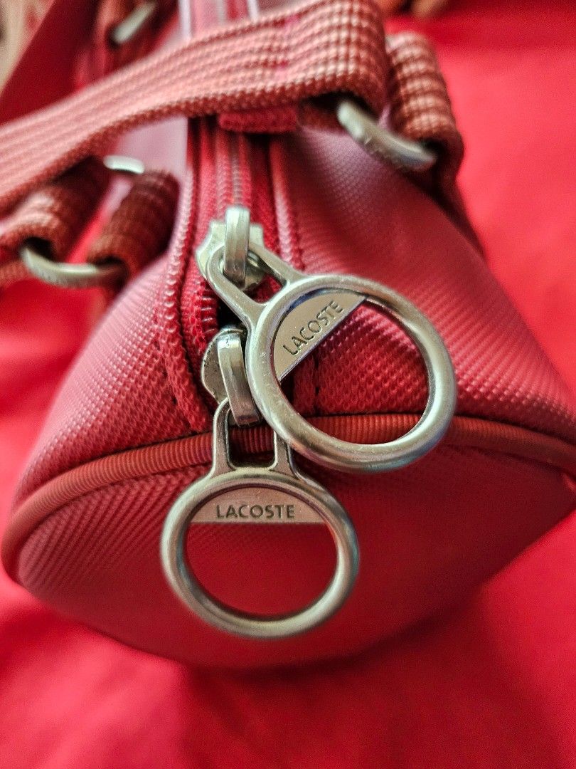 Lacoste Red Shoulder Barrel Bag (Category: Shoulder Bags) located in Mandaluyong City. Submitted by ohwmaria (Listing ID 1465617599, Image 3). Description: - Authentic red Lacoste barrel bag in vibrant nylon exterior - Sturdy structured handles and durable woven shoulder straps - Dual zipper closure with branded metal pulls - Classic embroidered green alligator logo on the side - Green and white striped fabric inner lining with a handy small clas