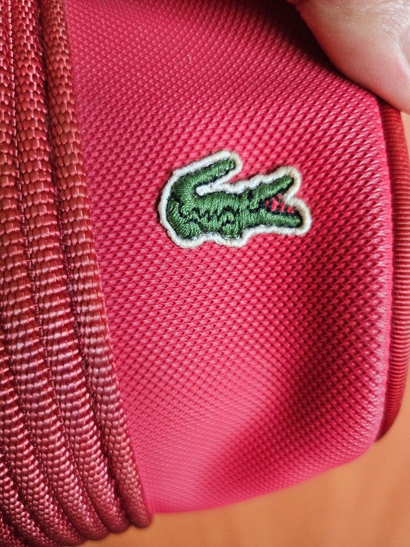 Lacoste Red Shoulder Barrel Bag (Category: Shoulder Bags) located in Mandaluyong City. Submitted by ohwmaria (Listing ID 1465617599, Image 2). Description: - Authentic red Lacoste barrel bag in vibrant nylon exterior - Sturdy structured handles and durable woven shoulder straps - Dual zipper closure with branded metal pulls - Classic embroidered green alligator logo on the side - Green and white striped fabric inner lining with a handy small clas