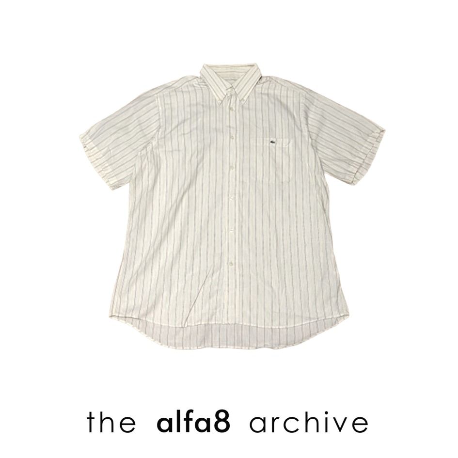 LACOSTE | Short Sleeve Striped Button Down Shirt Size 41 (Category: Tshirts & Polo Shirts ) located in Imus. Submitted by thealfa8archive (Listing ID 1465744274, Image 1). Description: - Brand: Lacoste - Style: Short-sleeve button-down shirt - Color/Pattern: Cream base with thin multicolored stripes (yellow, blue, red, grey) - Size: 41 (Tag at inner collar) - Features: Button-down collar, single chest pocket with iconic embroidered green crocodil