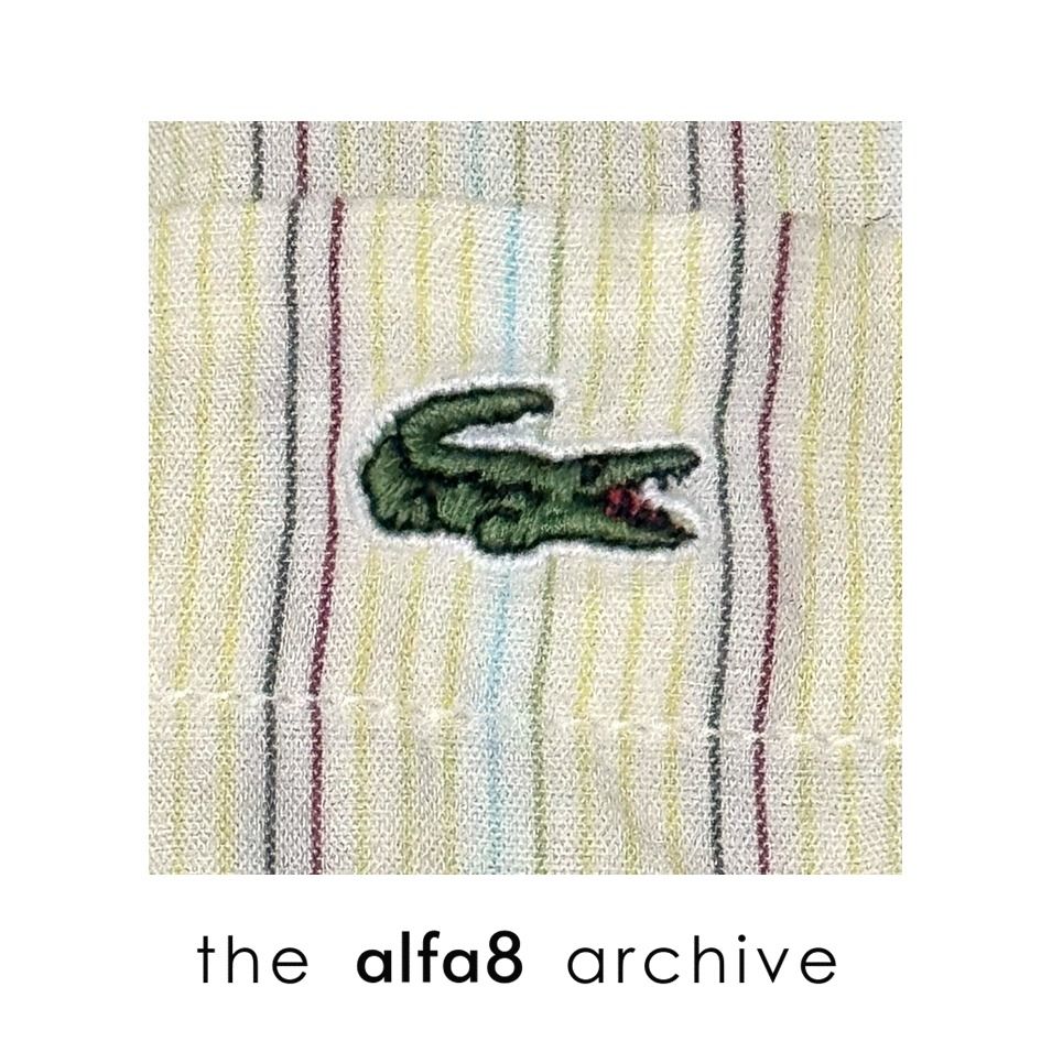 LACOSTE | Short Sleeve Striped Button Down Shirt Size 41 (Category: Tshirts & Polo Shirts ) located in Imus. Submitted by thealfa8archive (Listing ID 1465744274, Image 3). Description: - Brand: Lacoste - Style: Short-sleeve button-down shirt - Color/Pattern: Cream base with thin multicolored stripes (yellow, blue, red, grey) - Size: 41 (Tag at inner collar) - Features: Button-down collar, single chest pocket with iconic embroidered green crocodil