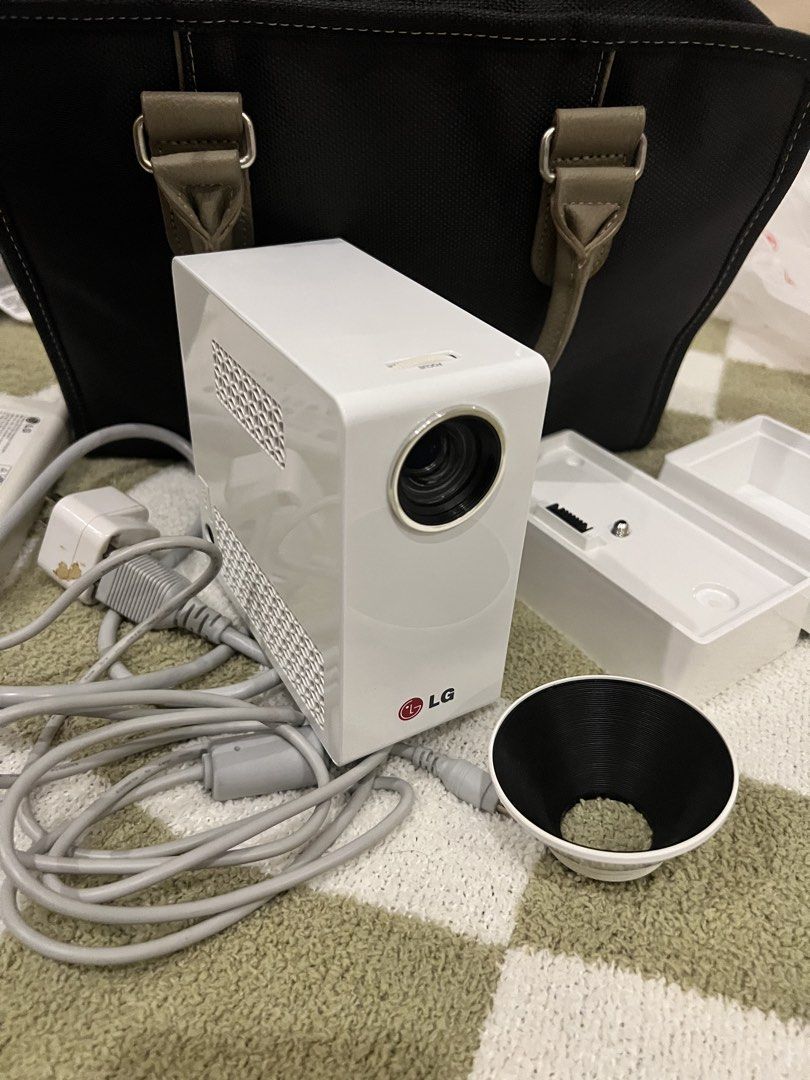 LG PG65U Mini Projector with Power Adapter and Stand (Category: Projectors) located in Bacoor. Submitted by jyano (Listing ID 1465667536, Image 2). Description: - Model: LG PG65U LED Projector in a sleek white casing - Includes power adapter with cables, detachable stand base, and lens attachment cone - Compact vertical design featuring honeycomb ventilation panels on the side and top - Powered via external brick charger with model details on the