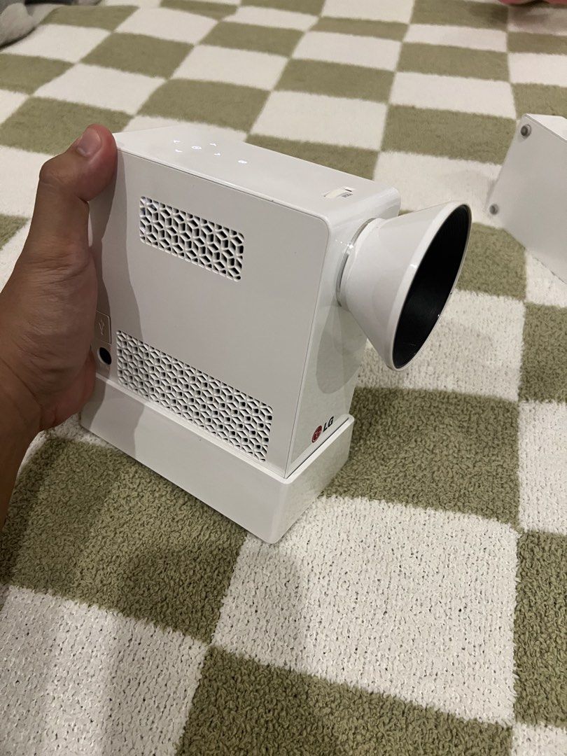 LG PG65U Mini Projector with Power Adapter and Stand (Category: Projectors) located in Bacoor. Submitted by jyano (Listing ID 1465667536, Image 1). Description: - Model: LG PG65U LED Projector in a sleek white casing - Includes power adapter with cables, detachable stand base, and lens attachment cone - Compact vertical design featuring honeycomb ventilation panels on the side and top - Powered via external brick charger with model details on the