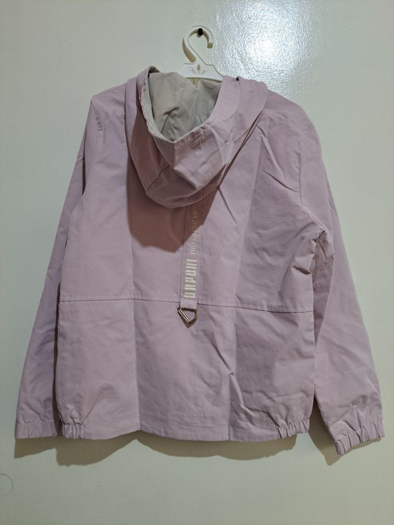 Light Pink Zip Up Hooded Windbreaker Jacket (Category: Coats, Jackets and Outerwear) located in Manila. Submitted by yselles__ (Listing ID 1465604315, Image 3). Description: - Color: Light pink - Style: Zip-up hoodie with smooth, lightweight inner lining - Features: Front pockets with button details, elastic cuffs and hem - Details: Cute print on the chest and unique back strap design - Condition: Clean, worn just a few times.