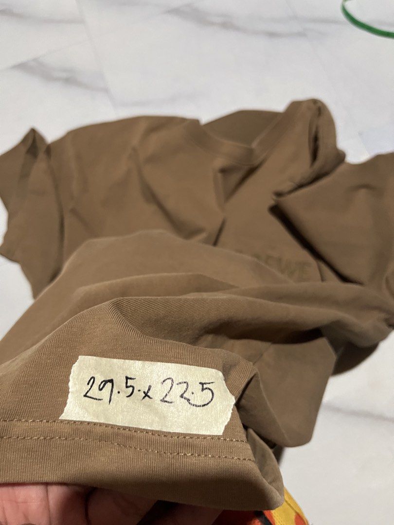 Loewe Brown Anagram Pocket Tee Size L (Category: Shirts) located in Cavite. Submitted by christianzuuu (Listing ID 1465727224, Image 3). Description: - Brand: Loewe - Color: Brown - Material: 100% Cotton (Made in Portugal) - Size: Large (tag attached at collar) - Design: Chest pocket with embroidered anagram logo and brand lettering - Measurements: Approx. 29.5" length x 22.5" width - Condition: Excellent / Pre-loved .