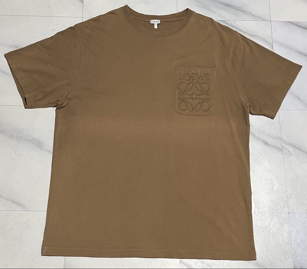 Loewe Brown Anagram Pocket Tee Size L (Category: Shirts) located in Cavite. Submitted by christianzuuu (Listing ID 1465727224, Image 1). Description: - Brand: Loewe - Color: Brown - Material: 100% Cotton (Made in Portugal) - Size: Large (tag attached at collar) - Design: Chest pocket with embroidered anagram logo and brand lettering - Measurements: Approx. 29.5" length x 22.5" width - Condition: Excellent / Pre-loved .