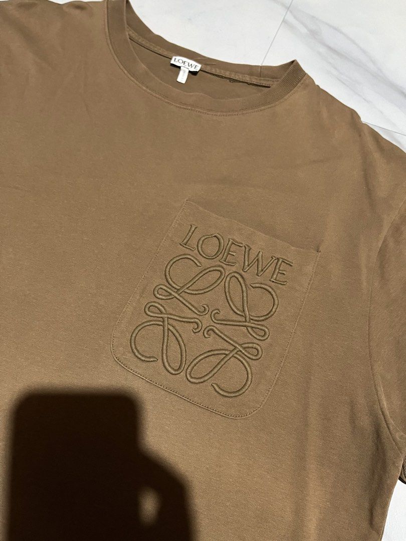 Loewe Brown Anagram Pocket Tee Size L (Category: Shirts) located in Cavite. Submitted by christianzuuu (Listing ID 1465727224, Image 2). Description: - Brand: Loewe - Color: Brown - Material: 100% Cotton (Made in Portugal) - Size: Large (tag attached at collar) - Design: Chest pocket with embroidered anagram logo and brand lettering - Measurements: Approx. 29.5" length x 22.5" width - Condition: Excellent / Pre-loved .
