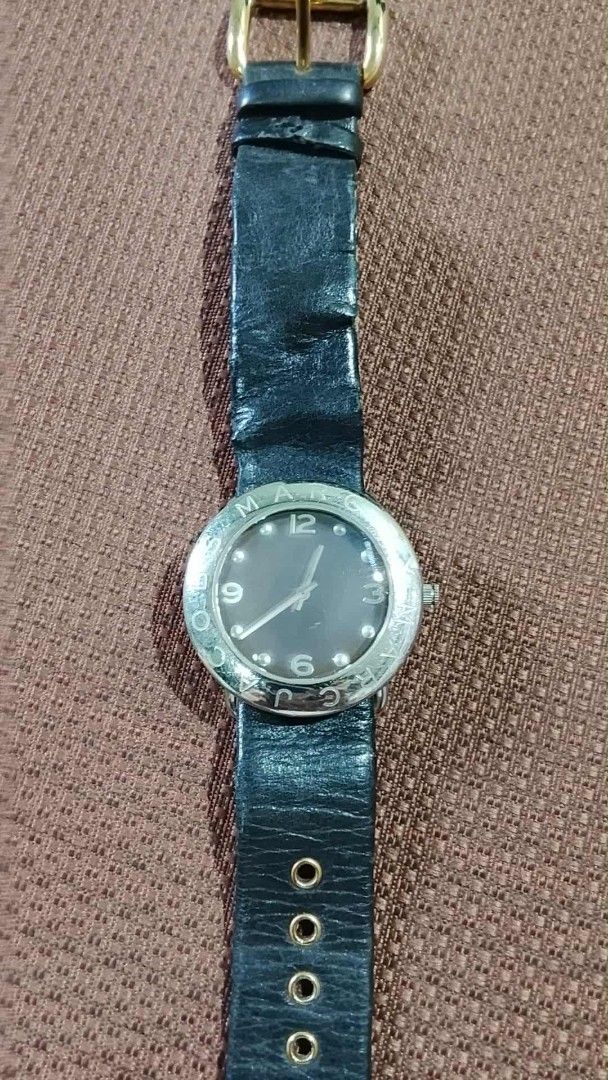 Marc Jacobs analog wristwatch with black leather strap (Category: Women's Watches) located in Bacoor. Submitted by lothea618 (Listing ID 1465614502, Image 1). Description: - Brand: Marc Jacobs - Dial: Dark round face with numeric markers at 3, 6, 9, and 12 - Bezel: Silver-tone with engraved brand lettering - Strap: Black leather with visible creases/wear and extra punched eyelets - Hardware: Gold-tone buckle.