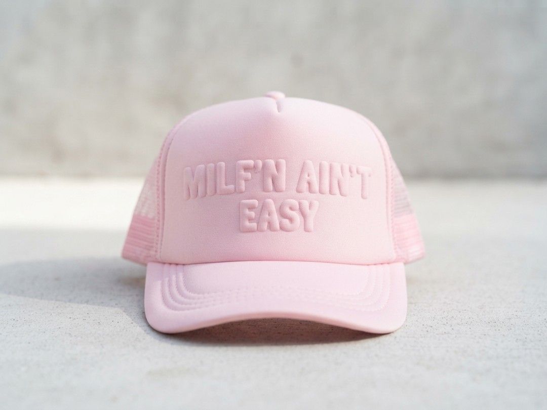Milf'n Ain't Easy" Pink Trucker Hat (Category: Hats & Beanies) located in Binangonan. Submitted by yuristalin888 (Listing ID 1465583728, Image 1). Description: * **Design:** Features a bold "MILF'N AIN'T EASY" slogan embossed on a matching pink foam front panel. * **Structure:** Classic trucker hat style designed with a structured front, breathable pink mesh back and side panels, and a curved brim with stitched detailing. * **Fit & Comfort:** Bui