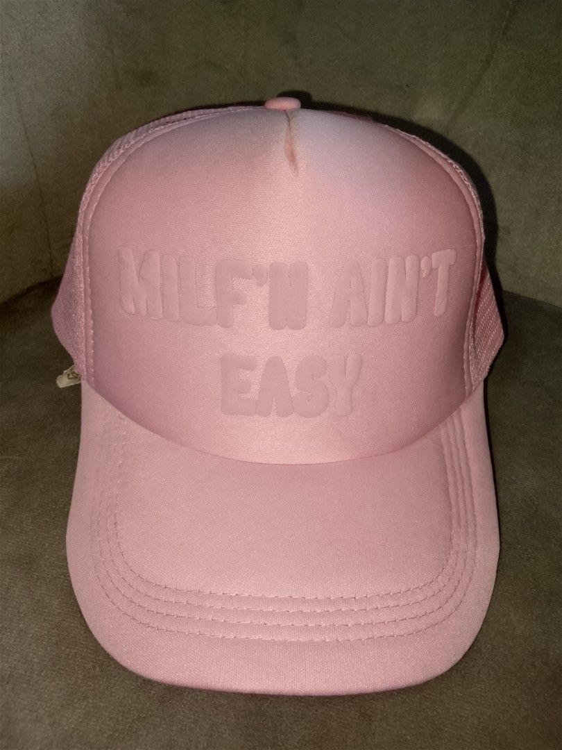 Milf'n Ain't Easy" Pink Trucker Hat (Category: Hats & Beanies) located in Binangonan. Submitted by yuristalin888 (Listing ID 1465583728, Image 2). Description: * **Design:** Features a bold "MILF'N AIN'T EASY" slogan embossed on a matching pink foam front panel. * **Structure:** Classic trucker hat style designed with a structured front, breathable pink mesh back and side panels, and a curved brim with stitched detailing. * **Fit & Comfort:** Bui