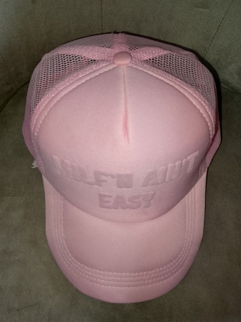 Milf'n Ain't Easy" Pink Trucker Hat (Category: Hats & Beanies) located in Binangonan. Submitted by yuristalin888 (Listing ID 1465583728, Image 3). Description: * **Design:** Features a bold "MILF'N AIN'T EASY" slogan embossed on a matching pink foam front panel. * **Structure:** Classic trucker hat style designed with a structured front, breathable pink mesh back and side panels, and a curved brim with stitched detailing. * **Fit & Comfort:** Bui