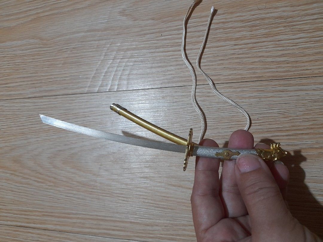 Miniature Katana (Category: Vintage Collectibles) located in Bocaue. Submitted by marajapansurplus (Listing ID 1465695247, Image 2). Description: - Miniature samurai sword replica for display - Silver blade with gold-tone guard, handle, and scabbard - Detailed lion or beast pommel design with small tassel - Attached white cord for easy hanging - Clean condition with no major marks or scratches - selling as it is.