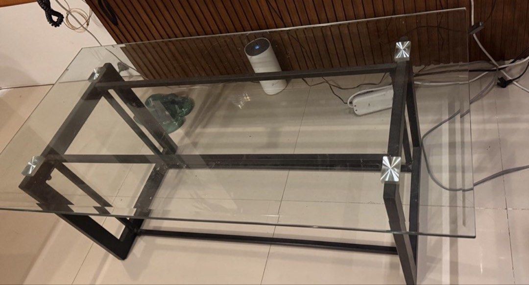 Modern glass top coffee table with dark metal frame (Category: Tables & Sets) located in Quezon City. Submitted by anastoreonline (Listing ID 1465582874, Image 2). Description: - Modern industrial style rectangle coffee table - Clear glass top with secure silver corner accents - Sturdy dark metal geometric legs - Clean lines and minimal design - Versatile piece that fits most living rooms - Condition: Excellent / Well-maintained - Meet-up or deli