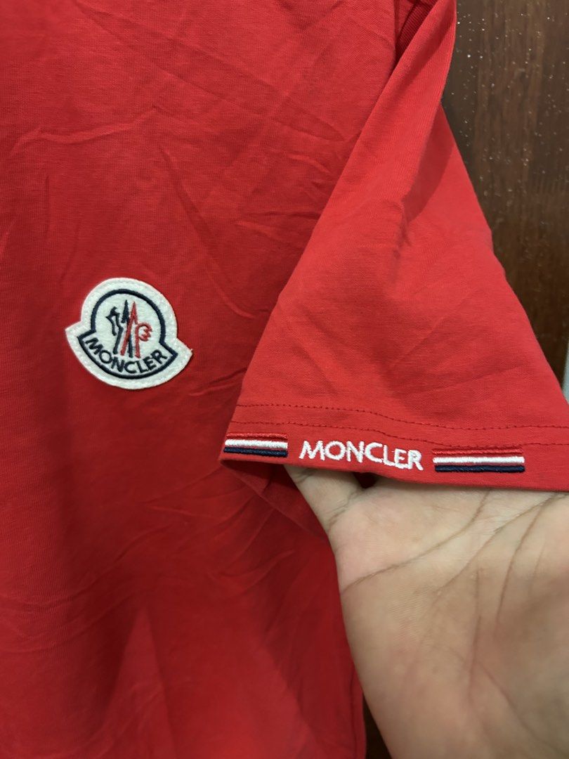 Moncler Red T-Shirt Size S (Category: Tshirts & Polo Shirts ) located in Davao. Submitted by ruggedthrift444 (Listing ID 1465687165, Image 3). Description: Red Moncler cotton t-shirt in size small. Features the classic Moncler logo patch on the chest. Has branded sleeve detailing with tricolor striping on the cuffs. Tag shows Moncler USA Inc. labeling and made in Italy details. Inner neck tag has some yellowing discoloration marks visible..