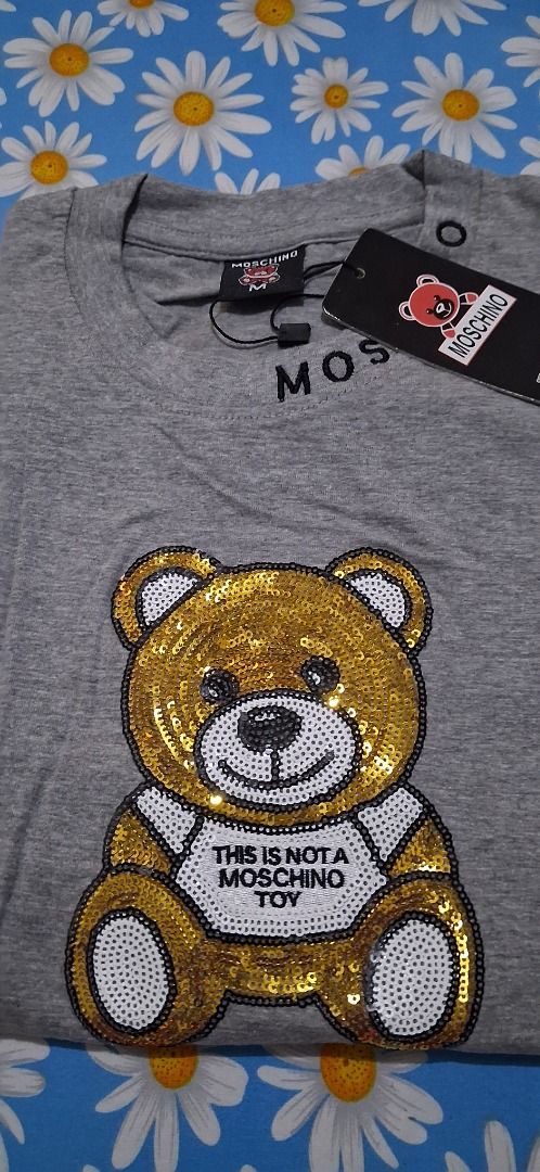 Moschino Grey Sequin Teddy Bear T-Shirt (Category: Shirts) located in Manila. Submitted by katkween23 (Listing ID 1465634075, Image 3). Description: - Brand new with tags (BNWT) - Color: Grey - Material: 100% Cotton - Fit: Regular crew neck, short sleeves - Details: Signature Moschino lettering on the neckline - Design: Eye-catching large sequin teddy bear graphic with 'This is not a Moschino toy' text.