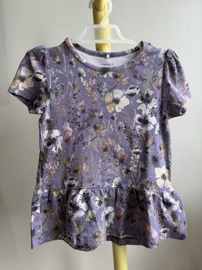 Name It Purple Floral Peplum Top (Category: Babies & Kids Fashion) located in Quezon City. Submitted by warmrabbit_414908 (Listing ID 1465594532, Image 2). Description: - Brand: Name It - Color: Dusty purple with all-over floral print - Size: Girls - Features: Short puff sleeves and cute ruffled peplum hem - Material: Soft cotton blend - Condition: Excellent, no stains or tears spotted - Perfect for everyday wear.