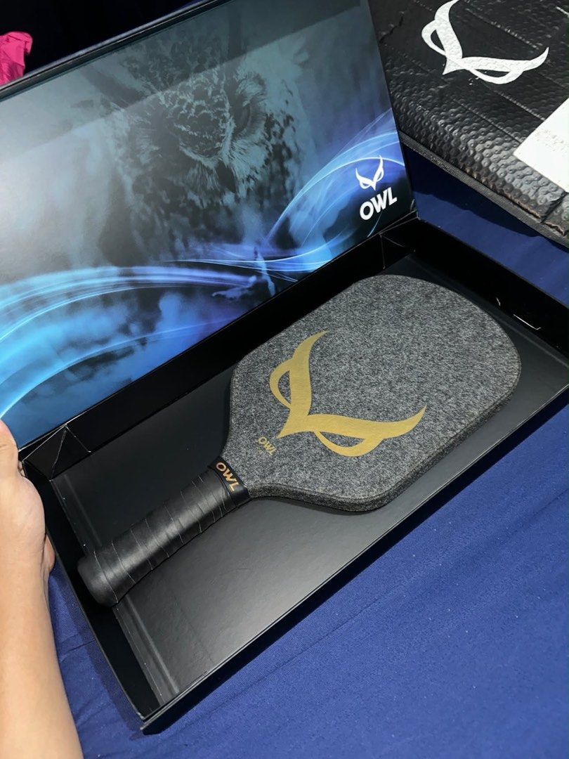 OWL CXE Pickleball Paddle with Box (Category: Racket and Ball Sports) located in Manila. Submitted by mariyaeleyn (Listing ID 1465746470, Image 3). Description: - Brand: OWL CXE - Condition: Used, kept safely stored in box - Design: Grey textured surface with striking gold owl logo - Handle: Black wrapped grip with gold branding - Inclusions: Original black presentation box with blue graphic inside - with receipt Forsale: The OWL CXE - Drew Brees