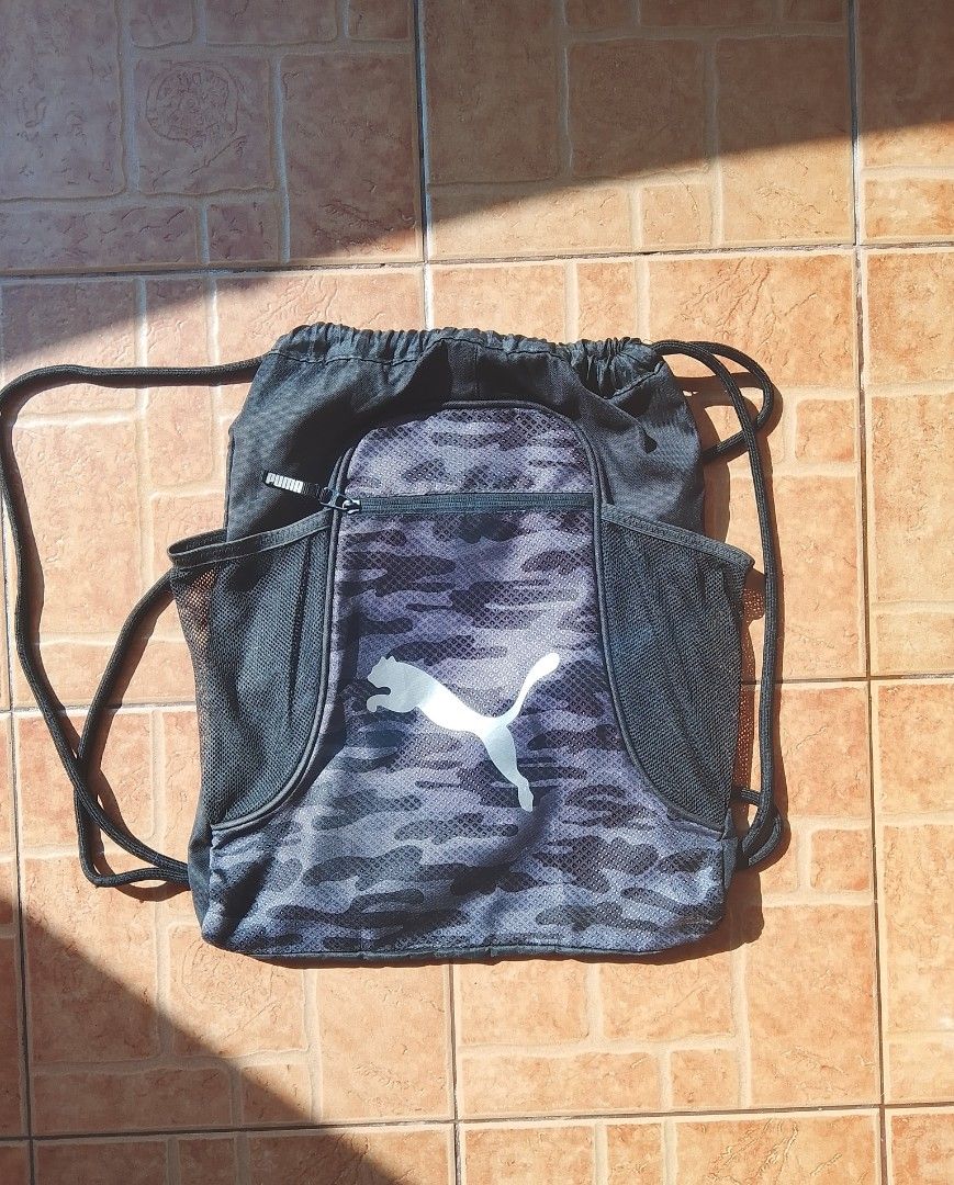Puma Black Camo Drawstring Backpack Gym Bag (Category: Backpacks) located in Cabuyao City. Submitted by kyokiiiiiii (Listing ID 1465581137, Image 1). Description: - Brand: Puma - Design: Grey camouflage front panel with a large white Puma cat logo - Storage: Front zippered pocket with branded pull tab and black mesh side pockets - Build: Durable drawstring cords on both sides - Usage: Ideal for gym gear, sports equipment, or everyday casual trips