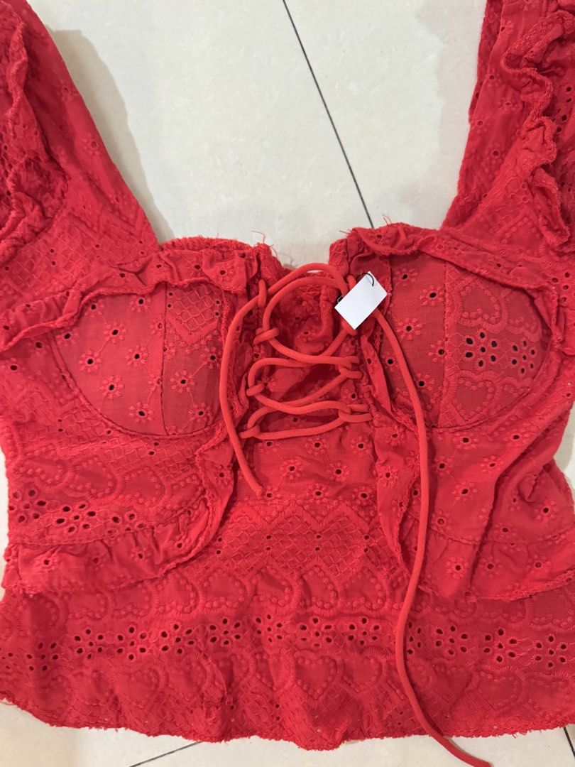Red eyelet lace corset crop top with ruffles whimsy (Category: Blouses) located in Quezon City. Submitted by sweetlyluxe (Listing ID 1465601384, Image 2). Description: - Color: Bright red with subtle heart patterns - Material: Lightweight eyelet embroidery fabric - Design: Front lace-up detail, corset-style bust cups, short ruffle sleeves, and flared hem - Closure: Exposed silver zipper at the back - Style: Summery and trendy crop top for birthda