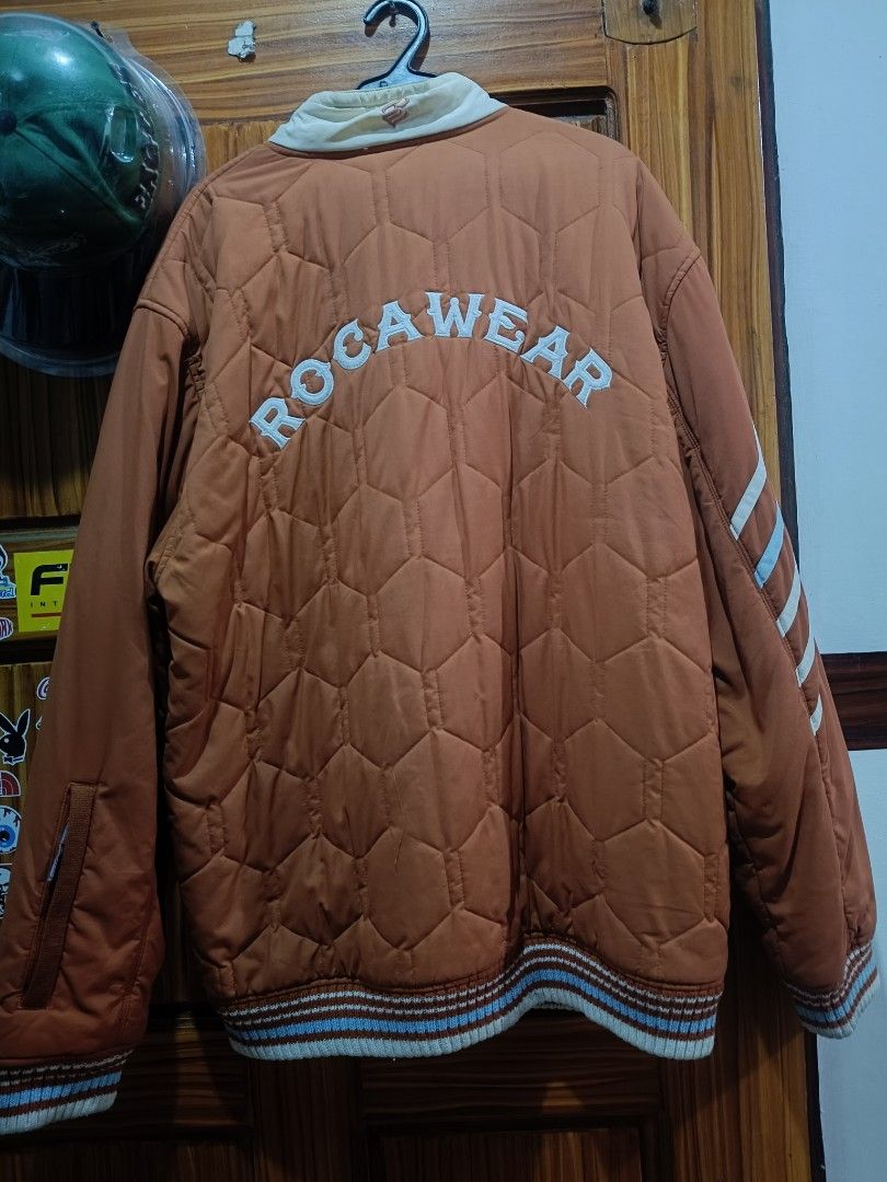 Rocawear Quilted Bomber Jacket (Category: Coats, Jackets and Outerwear) located in Marikina City. Submitted by pungs1800 (Listing ID 1465733858, Image 2). Description: - Brand: Rocawear - Style: Quilted bomber jacket in warm brown - Collar: High collar in contrast cream - Details: Bold embroidered logos on chest and back - Cuffs & Hem: Striped ribbed design - Pockets: Functional zipped sleeve pockets - Closure: Full front zip - Condition: Excelle