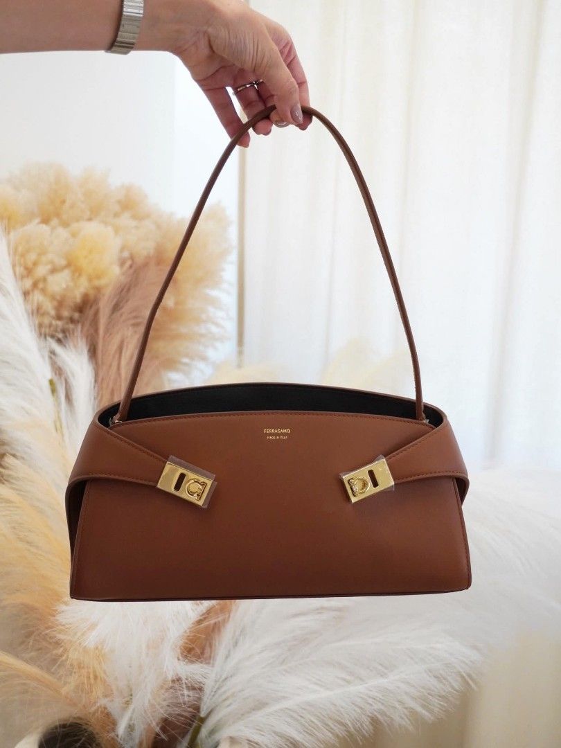 Salvatore Ferragamo Shoulder Bag (Category: Luxury Bags & Wallets) located in Paoay. Submitted by rvf1230 (Listing ID 1465649568, Image 1). Description: - Brand: Salvatore Ferragamo - Material: Rich brown leather with fabric lining - Style: Structured rectangular shoulder bag with slim top handle - Hardware: Gold-tone Gancini hardware (protective plastic film still attached) - Interior: Open main compartment with a secure zippered pocket and Ferr