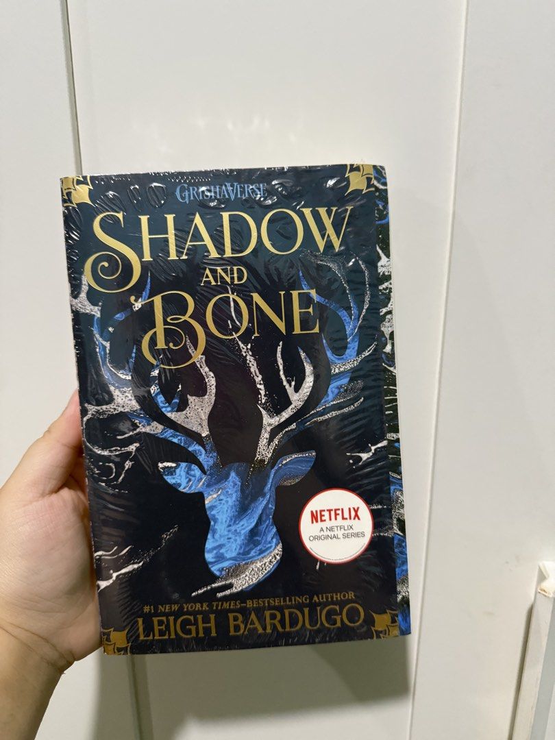 Shadow and Bone by Leigh Bardugo (BRAND NEW) (Category: Storybooks) located in Manila. Submitted by deanise_jil (Listing ID 1465735295, Image 1). Description: - Title: Shadow and Bone by Leigh Bardugo (Book 1 of the Grishaverse series) - Edition: Square Fish paperback with Netflix original series cover sticker - Condition: Brand new, still sealed tightly in original plastic wrapping (mild yellowing on pages/edges due to storage) - Extras: Include