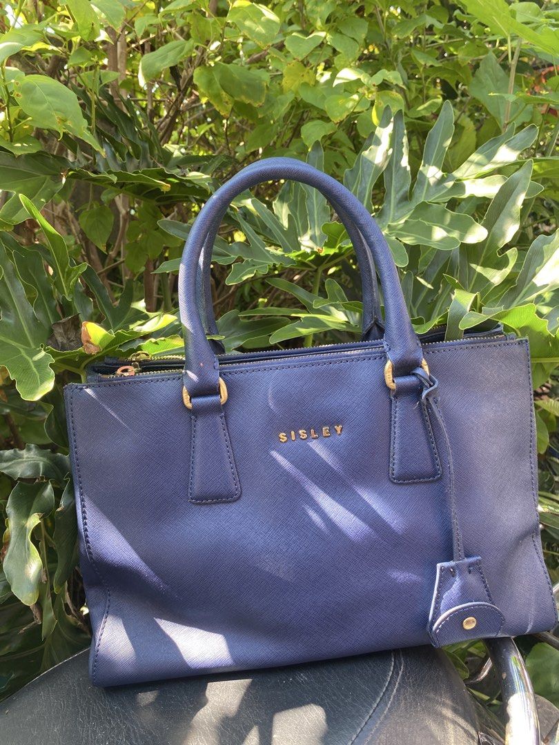 Sisley Blue Tote Handbag (Category: Tote Bags) located in Manila. Submitted by cdb_22 (Listing ID 1465595900, Image 1). Description: - Brand: Sisley - Color: Deep blue with gold hardware and lettering - Material: Textured faux leather - Closure: Secure top zipper - Handles: Double top handles with matching hanging key charm - Interior: Clean compartments - Usage: Perfect for daily use, work, or school.