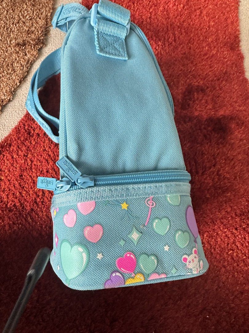Smiggle light blue heart pattern lunch bag with strap (Category: Babies & Kids Fashion) located in Imus. Submitted by mamibinkz (Listing ID 1465643686, Image 3). Description: - Smiggle double-decker lunch bag in light blue - Adorable all-over print featuring hearts, stars, and little cats - Double-decker zip compartment design for easy food organization - Adjustable shoulder strap with woven Smiggle logo - White Smiggle logo embroidered on the fr