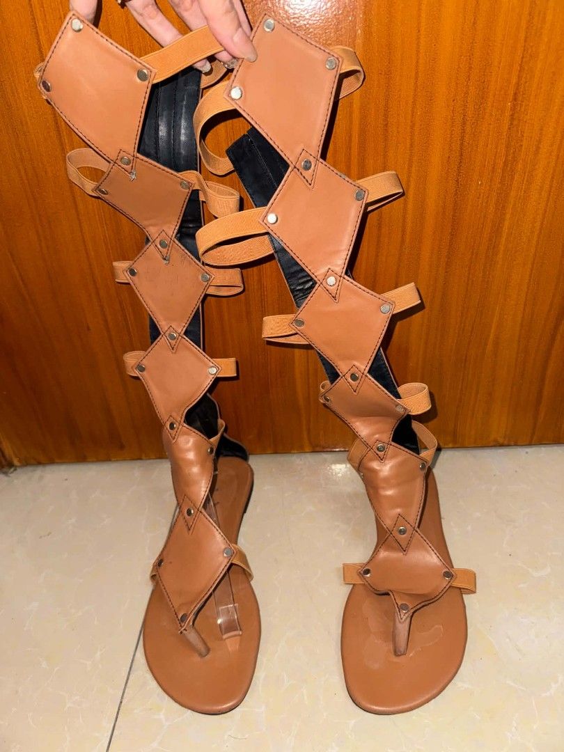 Tan Knee High Gladiator Sandals (Category: Flats & Sandals) located in Caloocan City. Submitted by mylove326 (Listing ID 1465684682, Image 2). Description: - Style: Knee-high gladiator sandals with geometric panels - Color/Accents: Tan with silver stud details and diamond-shaped cutouts - Fit: Thong toe post, flat sole, and elastic back straps for easy stretch and fit - Closure: Pull-on style shaft - Condition: Footbeds show normal signs of previ