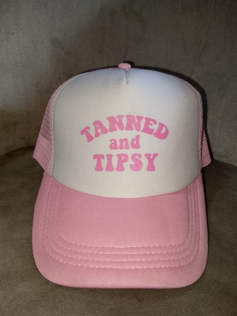 Tanned and Tipsy" Pink Trucker Hat (Category: Hats & Beanies) located in Binangonan. Submitted by yuristalin888 (Listing ID 1465583467, Image 2). Description: * **Design:** Features a playful "TANNED and TIPSY" slogan printed in bold pink lettering on a white foam front panel. * **Structure:** Classic trucker style combining a structured front, breathable pink mesh back and side panels, and a matching pink curved brim with stitched detailing. * *