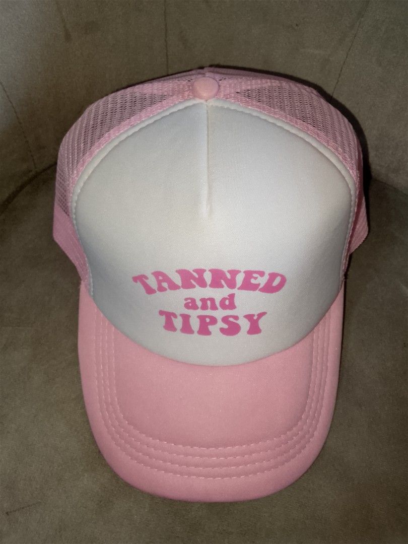 Tanned and Tipsy" Pink Trucker Hat (Category: Hats & Beanies) located in Binangonan. Submitted by yuristalin888 (Listing ID 1465583467, Image 3). Description: * **Design:** Features a playful "TANNED and TIPSY" slogan printed in bold pink lettering on a white foam front panel. * **Structure:** Classic trucker style combining a structured front, breathable pink mesh back and side panels, and a matching pink curved brim with stitched detailing. * *