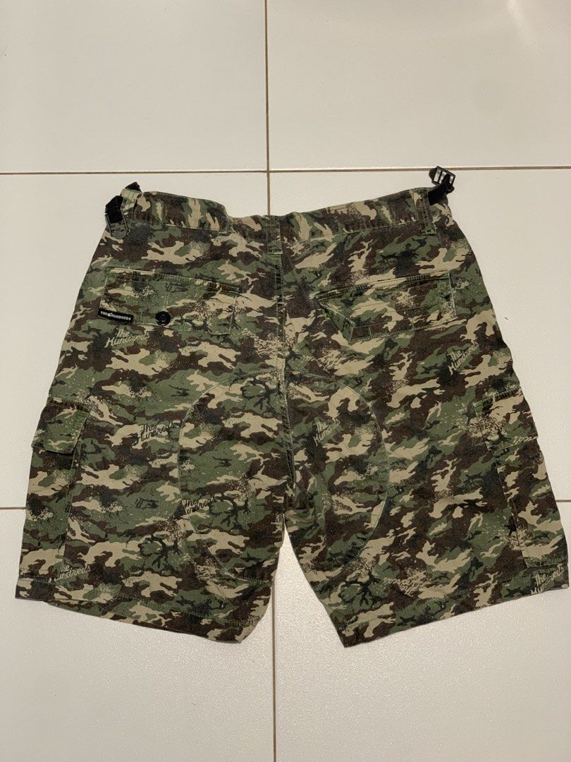 The Hundreds Camo Cargo Shorts (Category: Shorts) located in Mataasnakahoy. Submitted by grailsph.81630 (Listing ID 1465749851, Image 2). Description: - Brand: The Hundreds - Design: All-over camo print (green, brown, black) with subtle script logo accents - Storage: Multiple utility pockets with secure button closures on sides and back - Fit: Adjustable waist straps with metal buckles on both sides - Details: Button fly closure and branded inner