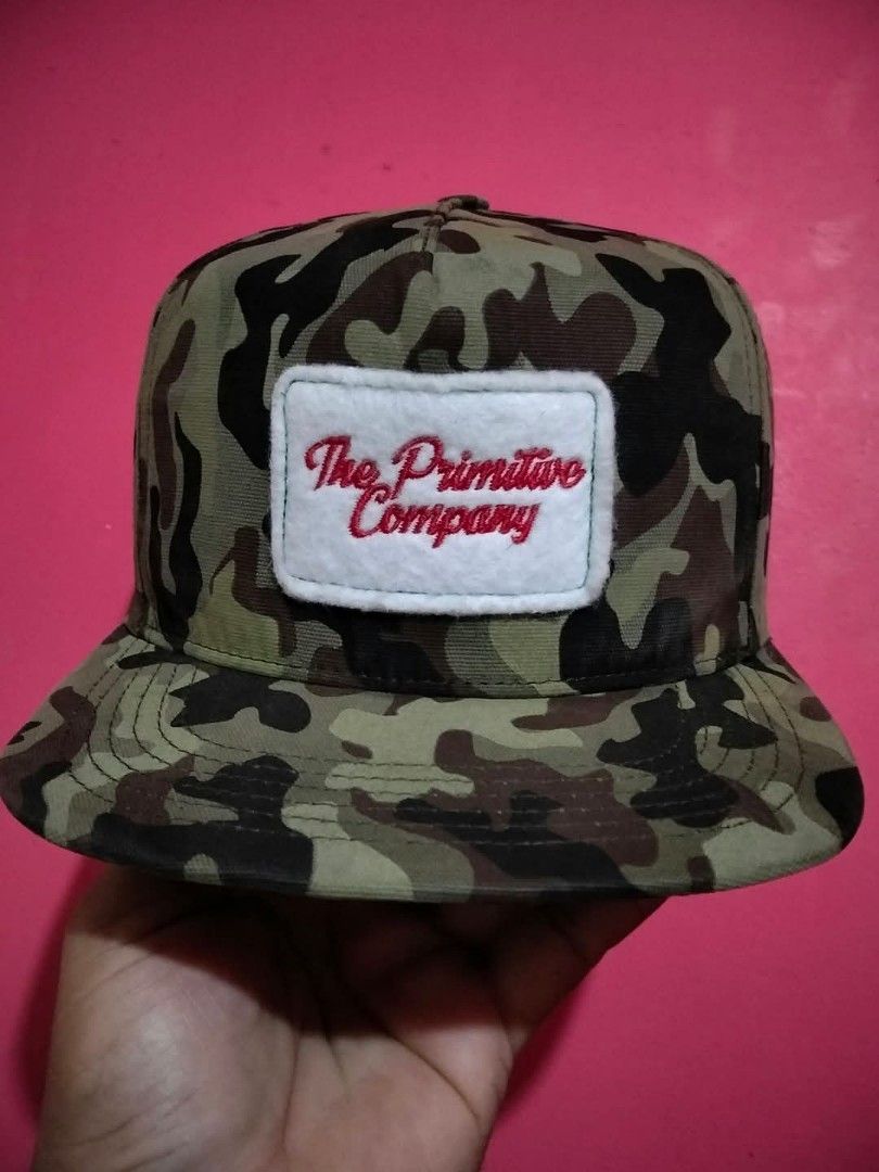 The Primitive Company Camouflage Snapback Cap (Category: Caps & Hats) located in Mangaldan. Submitted by niftythrifty69 (Listing ID 1465615232, Image 1). Description: - Brand: The Primitive Company - Design: Green camouflage with white felt patch and red embroidered script - Brim: Classic flat brim - Closure: Adjustable black plastic snapback with brand logo - Style: Streetwear essential, versatile for casual everyday wear - Condition: Excellent/