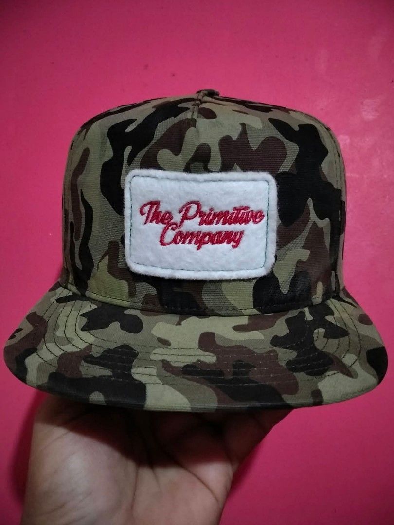The Primitive Company Camouflage Snapback Cap (Category: Caps & Hats) located in Mangaldan. Submitted by niftythrifty69 (Listing ID 1465615232, Image 2). Description: - Brand: The Primitive Company - Design: Green camouflage with white felt patch and red embroidered script - Brim: Classic flat brim - Closure: Adjustable black plastic snapback with brand logo - Style: Streetwear essential, versatile for casual everyday wear - Condition: Excellent/