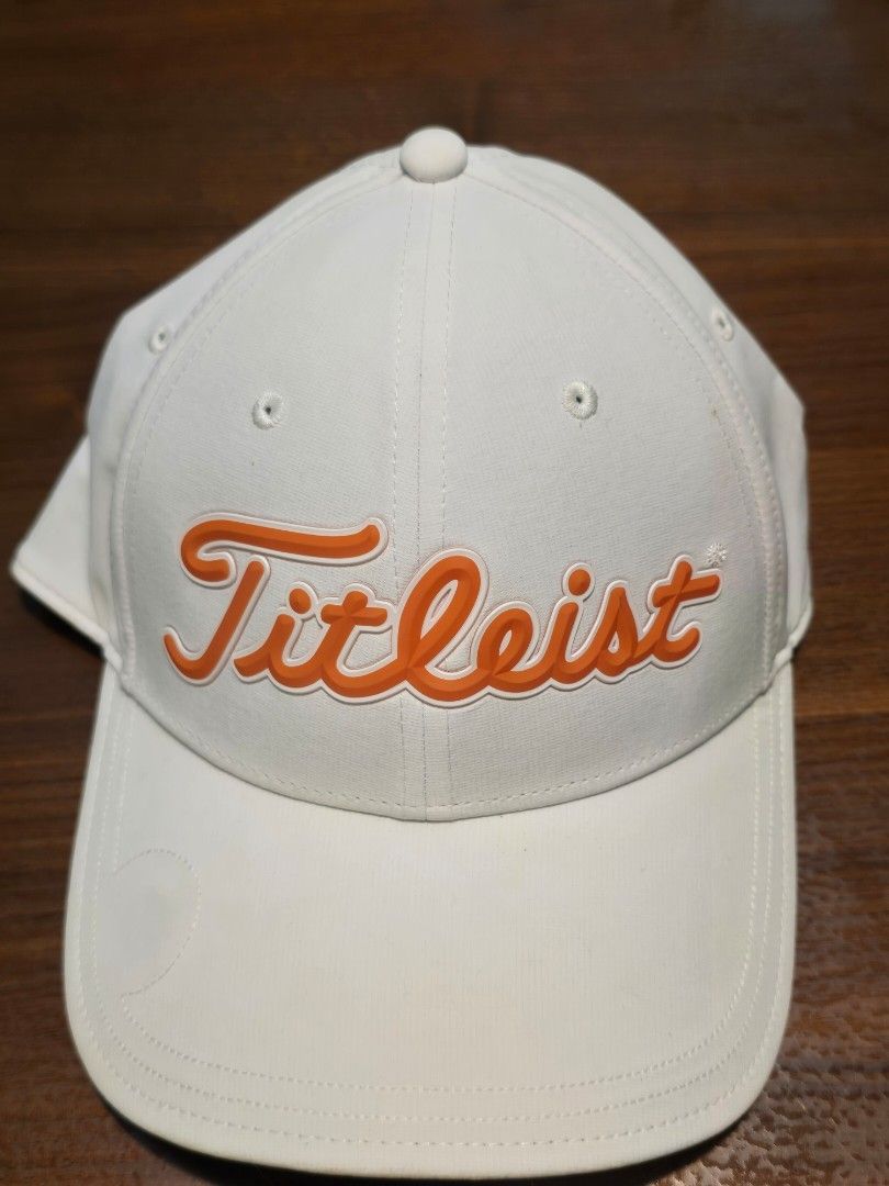 Titleist White Golf Cap with Orange Raised Logo (Category: Golf) located in San Juan City. Submitted by YardSaleSanJuan (Listing ID 1465655614, Image 1). Description: with magnet on visor - compatible with all metal ball markers - Brand: Titleist - Color: Clean white with bright orange raised front lettering - Style: Classic curved brim with stitched ventilation eyelets - Fit: Adjustable back strap for a custom fit - Perfect for golf, sports, or 