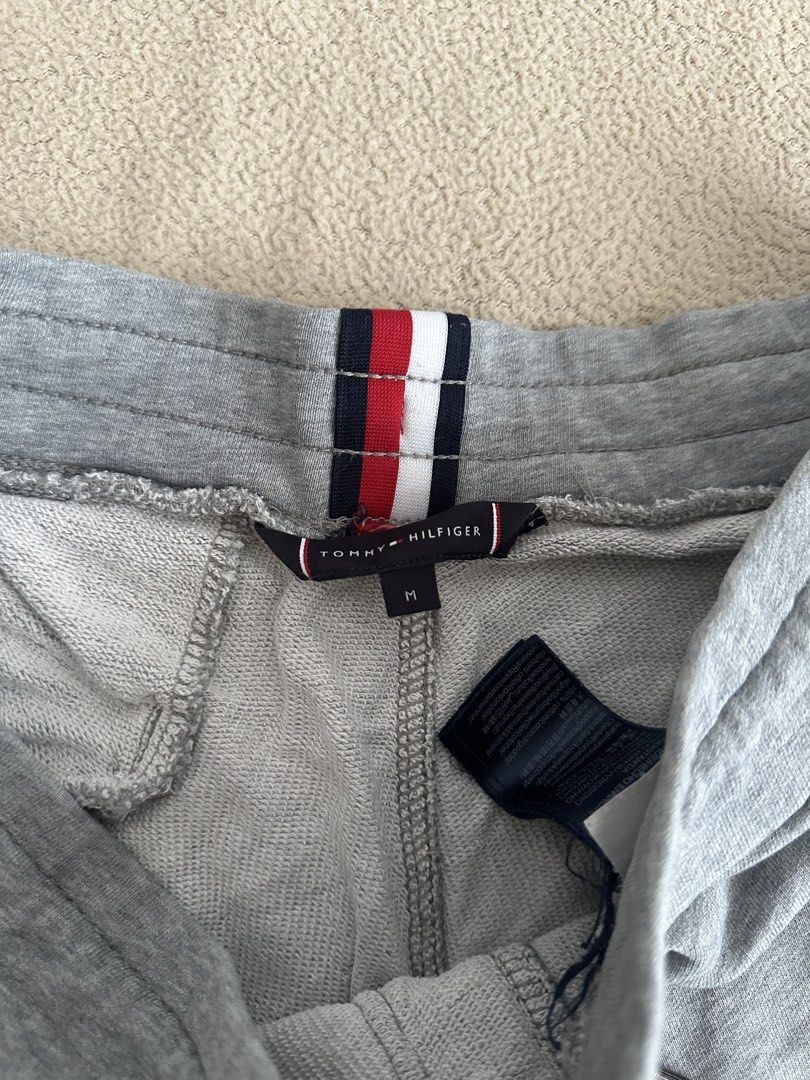 Tommy Hilfiger Grey Sweatpants Size M (Category: Joggers) located in Paranaque City. Submitted by kasheeko (Listing ID 1465620702, Image 3). Description: - Brand: Tommy Hilfiger - Color: Grey - Size: Medium (M) - Design: Large printed logo with 'Est. 1985' on the left leg - Waist: Drawstring waist with branded aglets and signature flag loop at the back - Pockets: One back pocket with tiny flag logo tag - Fit: Cuffed ankles for a snug look.