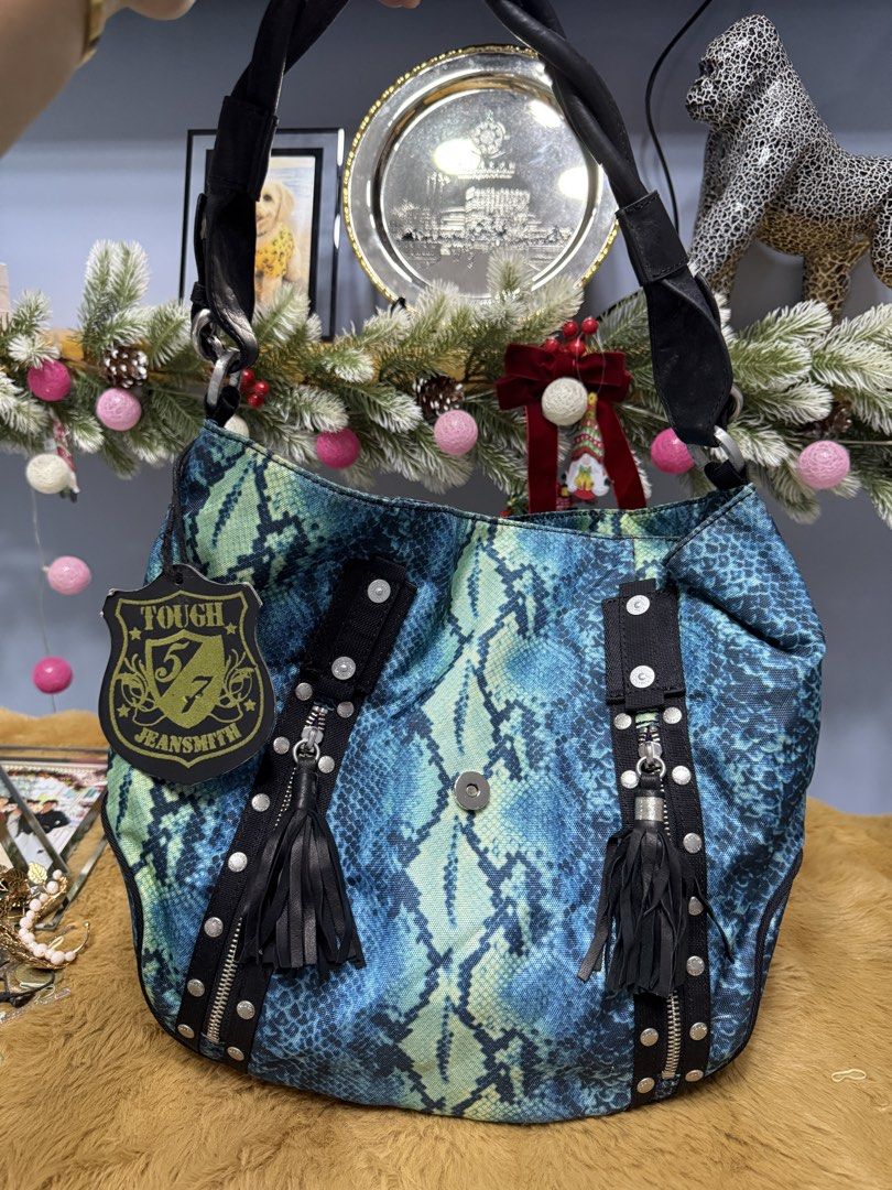 Tough Jeansmith Blue Snake Print Shoulder Bag (Category: Shoulder Bags) located in Alaminos. Submitted by jhean1323 (Listing ID 1465584878, Image 1). Description: - Brand: Tough Jeansmith - Design: Blue and green snake print with black leather trim - Details: Silver studs and stylish hanging tassels on front zippers - Closure: Secure magnetic button on the front - Interior: Vibrant purple fabric lining with built-in zipper compartments and slip p