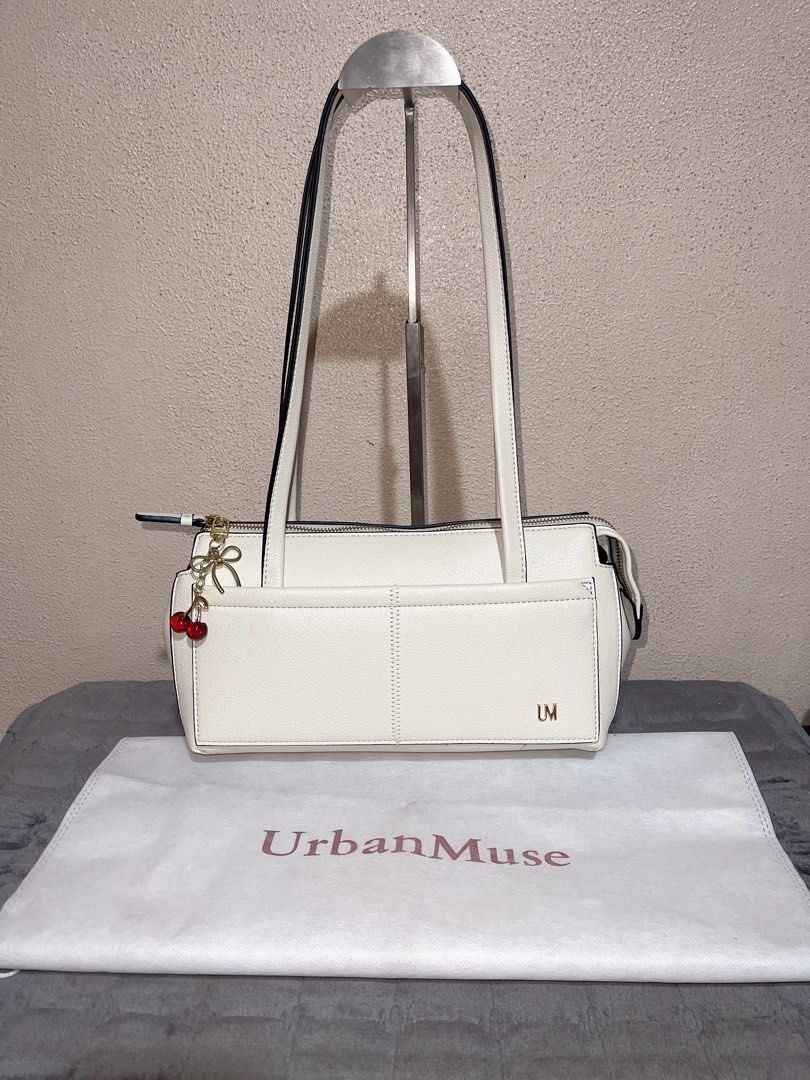 UrbanMuse White Shoulder Bag with Cherry Charm (Category: Shoulder Bags) located in Quezon City. Submitted by donnabelle7572 (Listing ID 1465668232, Image 1). Description: White leather-look shoulder bag from UrbanMuse. Gold zipper closure on top, double shoulder straps, structured rectangular shape. Outside pocket spans the front width, finished with gold-tone 'UM' lettering in the corner. Attached gold bow and red cherry keychain dangling from 