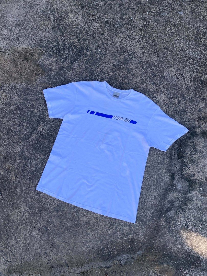 Vintage Nike White Blue Graphic Tee (Category: Tshirts & Polo Shirts ) located in Calabanga. Submitted by 4405.curator (Listing ID 1465594463, Image 2). Description: White Nike t-shirt with a blue graphic stripe and bold logo across the chest. Crew neckline, short sleeves. Size XL, made in Mexico. Classic retro look from the silver tag era. Got a few tiny faint marks near the front graphic stripe, check the close-up photo. Fabric feels well-worn 