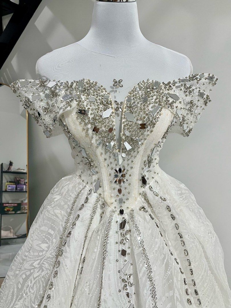 Wedding Gown (Category: Evening dresses & gowns) located in Manila. Submitted by macloset11 (Listing ID 1465655136, Image 1). Description: - Style: White ball gown wedding dress - Neckline: Off-shoulder with short sleeves and plunging sweetheart illusion panel - Bodice: Structured design featuring visible boning - Embellishments: Heavy silver rhinestones and mirrors across the bodice and down the skirt - Fabric: Textured patterned fabric that spa