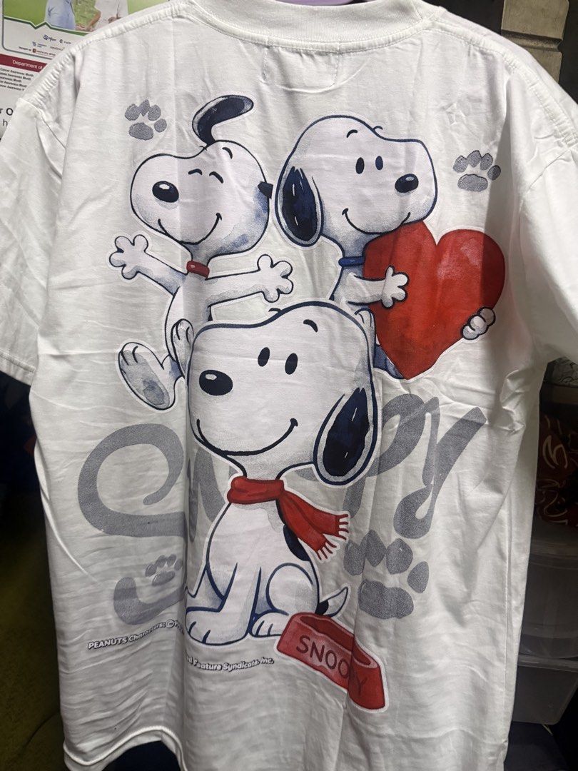 White Snoopy graphic tee with doghouse design (Category: Shirts) located in Manila. Submitted by smlumanog (Listing ID 1465598755, Image 2). Description: - Brand/Origin: Apple Pie, Made in Thailand - Design: Snoopy sitting on his doghouse with large grey textured 'Snoopy' lettering - Accent: Woodstock graphic near the right shoulder - Fit/Style: Classic round neckline and short sleeves - Condition: Clean fabric with bright, vivid printed graphics