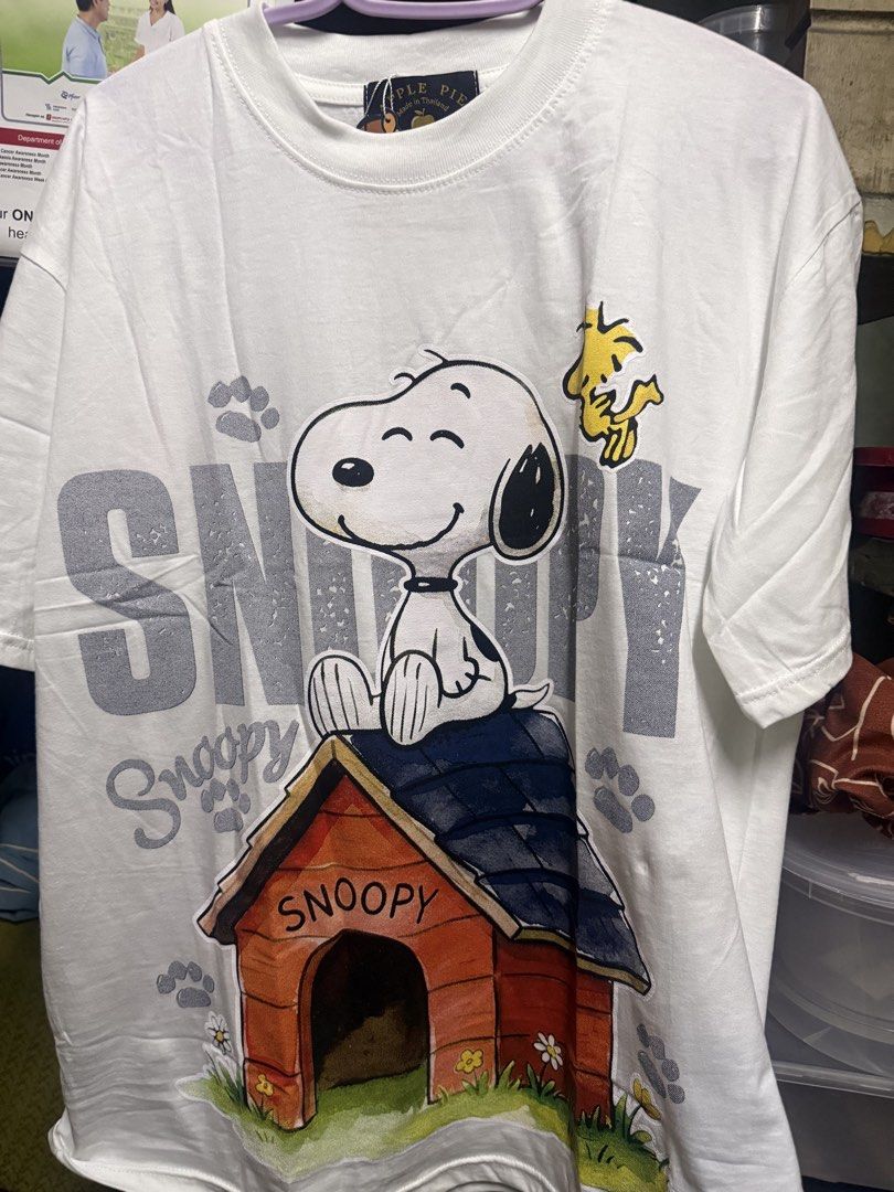 White Snoopy graphic tee with doghouse design (Category: Shirts) located in Manila. Submitted by smlumanog (Listing ID 1465598755, Image 1). Description: - Brand/Origin: Apple Pie, Made in Thailand - Design: Snoopy sitting on his doghouse with large grey textured 'Snoopy' lettering - Accent: Woodstock graphic near the right shoulder - Fit/Style: Classic round neckline and short sleeves - Condition: Clean fabric with bright, vivid printed graphics