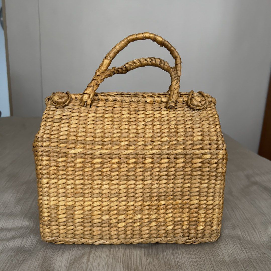 Woven Straw Handbag Structured Top Handle Basket Bag (Category: Beach Bags) located in Pasig City. Submitted by jenscloset86 (Listing ID 1465703700, Image 1). Description: • Natural woven straw handbag with a rigid structured shape and flat rectangular base. • Normal wear in one handle due to usage. • Double braided top handles with decorative knot accents and an open top. • Lightweight, easy to carry. • Perfect for summer! Measurement (in inches