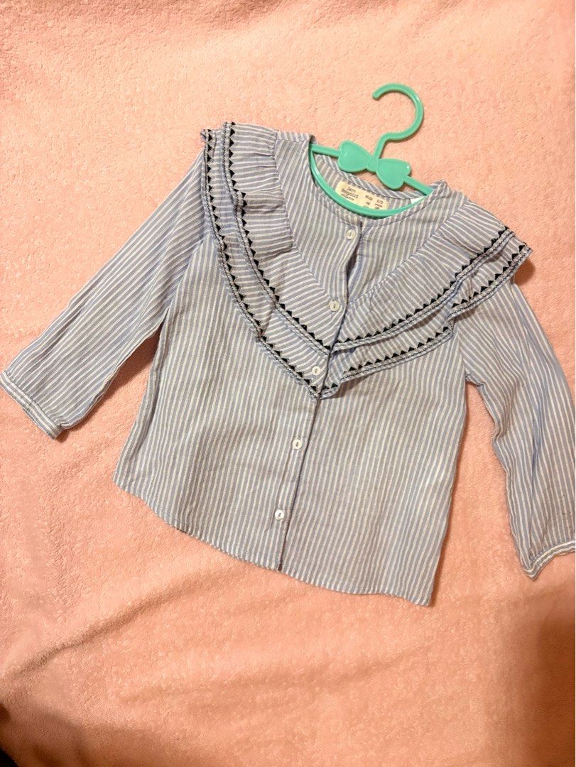 Zara Baby light blue and white vertical striped button-front blouse (Category: Babies & Kids Fashion) located in Quezon City. Submitted by closettreasure123 (Listing ID 1465597656, Image 1). Description: featuring a distinctive layered v-shaped ruffle collar with black geometric embroidered trim..