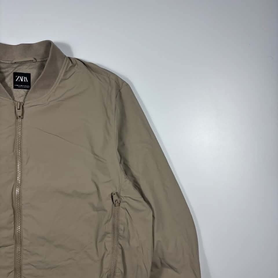 Zara Beige Bomber Jacket Size XXL (Category: Coats, Jackets and Outerwear) located in Manila. Submitted by kitkathrift (Listing ID 1465689321, Image 2). Description: - Brand: Zara - Style: Bomber Jacket - Color: Beige - Size: XXL (collar tag) - Closure: Full zip front - Pockets: 2 front zip exterior pockets + 1 interior zip pocket on the left - Details: Ribbed collar, cuffs, and hem, breathable mesh interior lining - Condition: Clean overall, no 